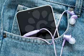 Smartphone with  earphones in the pocket of blue jeans