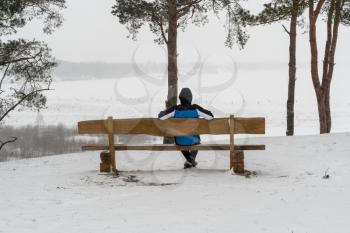 Man sitting on the bench in snowstorm,looking at the view