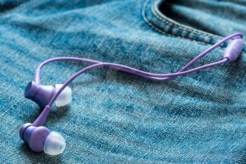 Purple earphones stick out of jeans pocket. The concept of music, sports, active lifestyle