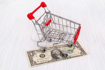 Shopping cart and one dollar on wooden surface.Money market.
