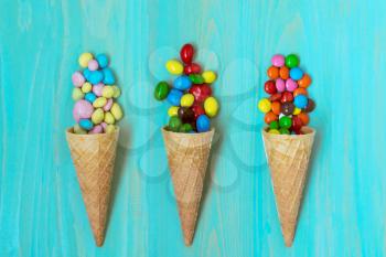 Three wafer cones with colored candy on wooden background