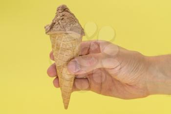 Ice cream cone in hand on yellow background. Summer desserts.
