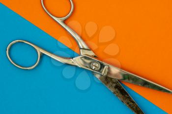 Metal scissors on orange and blue paper background