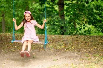 Little girl swinging on a sunny day with trees in the background