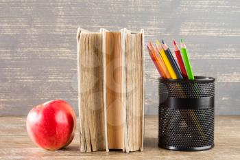 Books,apple and color pencils on wooden background