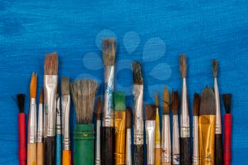 Set of dirty paint brushes on a blue painted canvas background