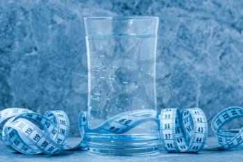 Glass of clean water with a measuring tape. Blue toned image