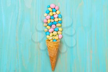Waffle cone with colored candy on a blue background. Top view, sweets and candy concept.