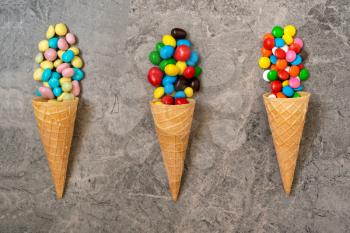 Waffle horns with colored candy on a stone background. Top view, sweets and candy concept.