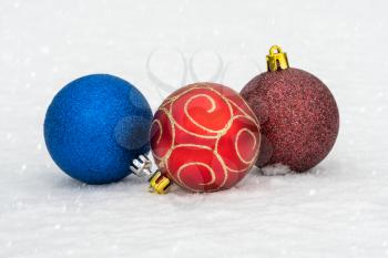 Three Christmas baubles on the snow with snowfall background