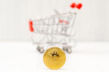 Bitcoin coin and blurry background with a shopping cart. Shopping cart with bitcoin as an investment concept