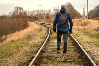 Man moves along railway tracks in the countryside. Rear view.