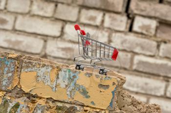 Shopping cart on the wall of dismantled building. Expenses for house building or renovation