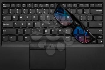 Black framed glasses on the computer keyboard, top view.