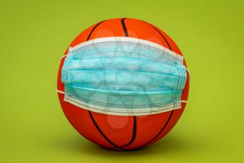 Basketball ball wearing surgical medical face mask. Concept for Coronavirus COVID 19 pandemic and epidemic affecting basketball seasons game suspend.