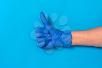 Hand in a blue rubber glove with thumb up on blue background