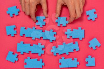 Concept of business,hands with a blue puzzle pieces on pink background.