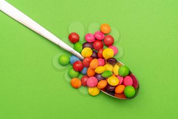 Metal spoon with multi-colored candies close up. Copy space.