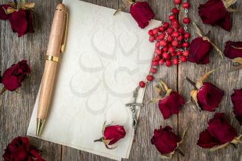 Dry roses, catholic rosary and blank letter on wooden background. Religious rosary on blank sheet of paper to write a letter