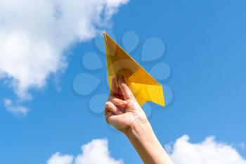 Child playing with toy airplane against blue summer sky background.