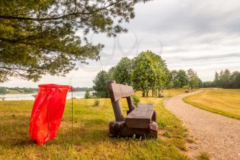 Wooden bench and plastic trash bag in the park. Ecology concept.