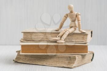 Wooden man sitting on the books stack. Literature research. Concept - information search in books. 