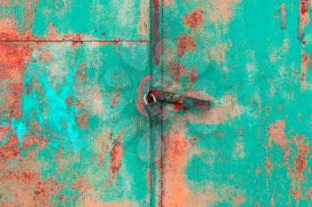 Old rusted grungy metal garage door with latch and padlock. Close up of rusty vintage lock on closed door