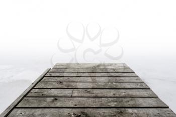 Pier into the fog. Wooden jetty on foggy day by the lakeside during winter.