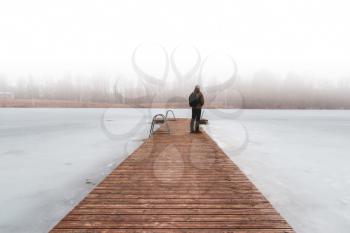 Man standing on a wooden bridge in the foggy morning. Beautiful freedom moment and peaceful atmosphere in nature. Back view.