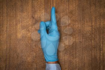 Male doctor hand in blue glove make gesture with index finger up.