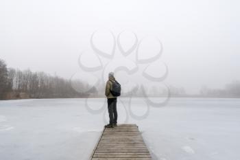 Man standing on a bridge in the fog. Wooden jetty on foggy day by the lakeside during winter.