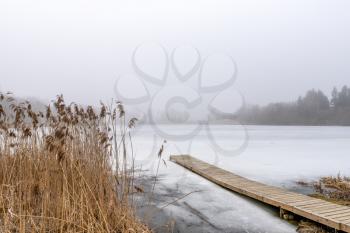 Wooden footbridge on lake with thick mist foggy air over frozen water.  Concepts: peaceful, mindfullness, secret, nature.