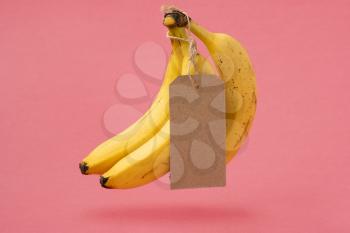 Bunch of bananas with a blank tag levitating on a pink background