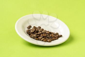 White plate with coffee beans over a green background