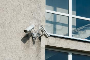 Two CCTV cameras on grey building wall with big windows