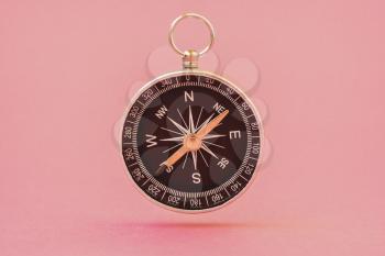 Black compass floating on the pink background