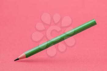 Green color pencil levitating over a pink background
