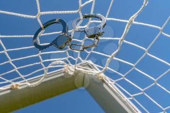 Scam with soccer or football gambling corruption. Handcuffs hanging on the net of a football goals