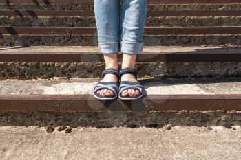 Womans leg in summer sandals stand on the concrete stairs. Girls comfortable summer shoes at city street