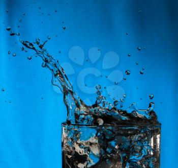 Water splash in glass on blue background