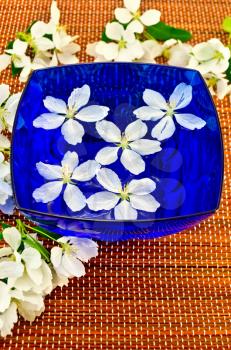 The white flowers of apple trees in the blue cup with water and brown bamboo mat