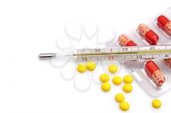 Thermometer with the yellow pills in bulk and red-white capsules in a package on a white background
