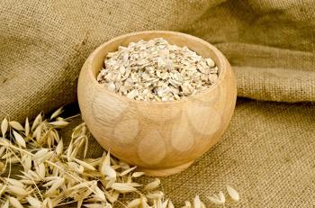 Oat flakes in a wooden bowl, stalks of oats on sackcloth and wooden board