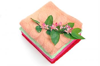 A pile of colorful towels, a sprig of pink flowers and green leaves on a white background