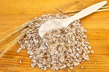 Rye flakes, wooden spoon and stalks of rye on a wooden board