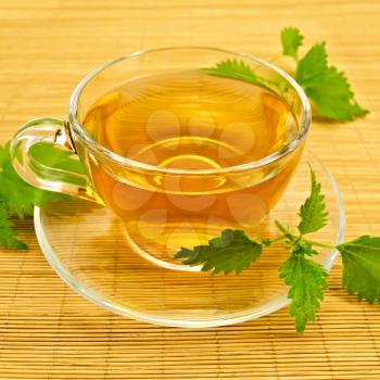 Herbal tea in a glass cup and saucer, three twig nettle on a bamboo napkin