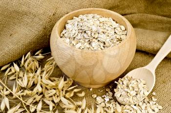 Oat flakes in a wooden bowl and spoon, stalks of oats on sackcloth and wooden board