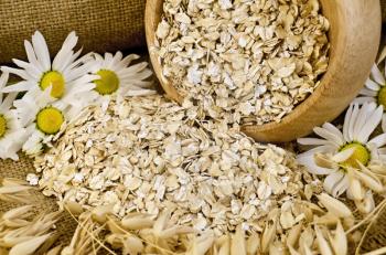 Oat flakes in a wooden bowl, stalks of oats, chamomile on sackcloth and wooden board