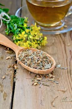 Wooden spoon with dried flowers tutsan, a bouquet of fresh flowers tutsan, glass cup with tea on a wooden boards background