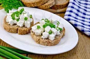 Slices of bread with feta cheese and chives on a plate, parsley, napkin on a wooden board